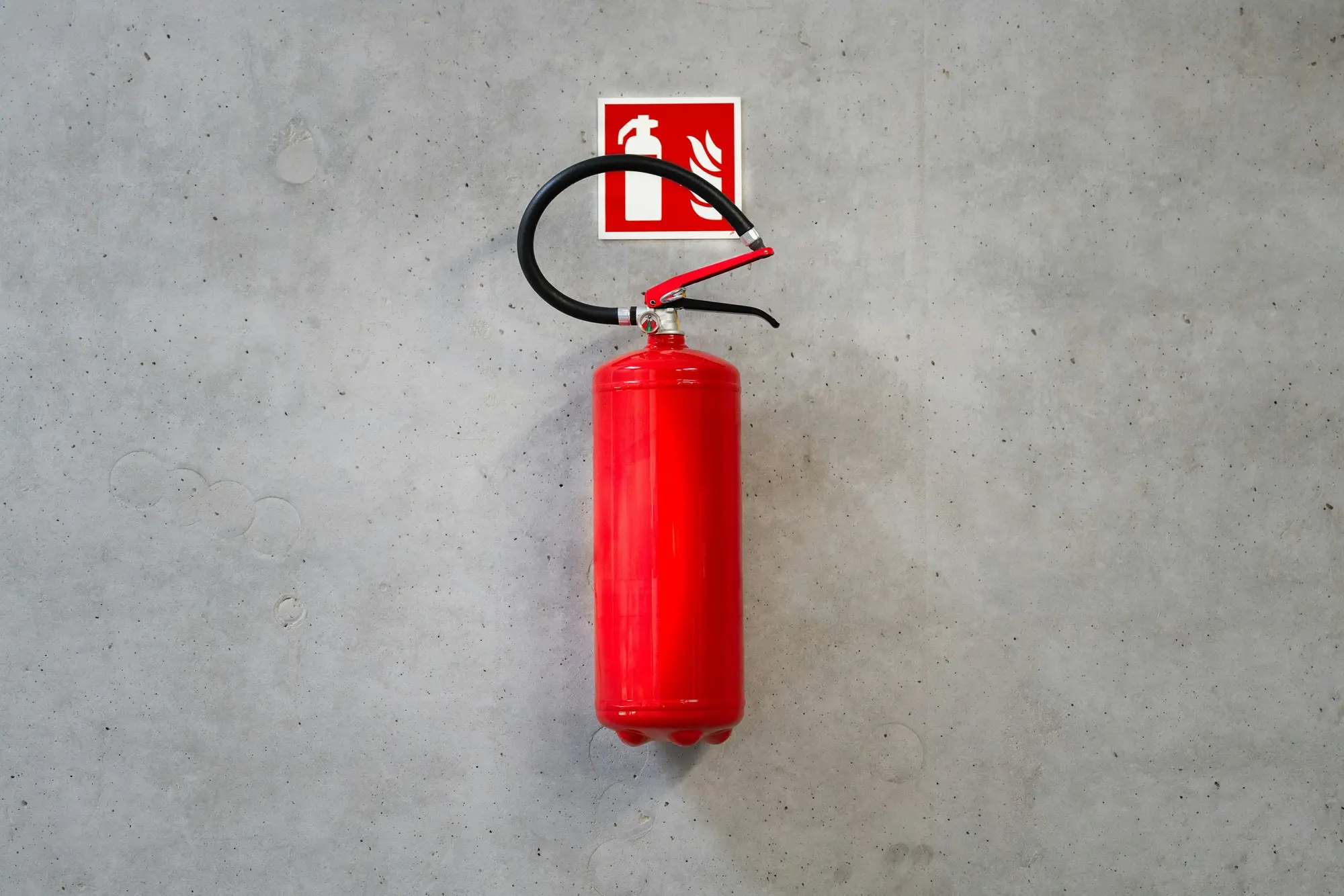 A red fire extinguisher hanging on a bare concrete wall below a red fire extinguisher sign.